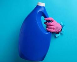 blue plastic bottle with liquid detergent in a female hand on a blue background. A part of the body sticks out of a torn hole in the background photo