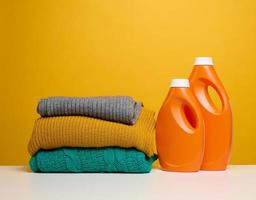 stack of washed folded clothes and plastic orange large bottles with liquid detergent stand on a white table, yellow background photo