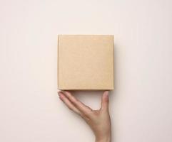 Female hand holding a square cardboard box on a beige background photo