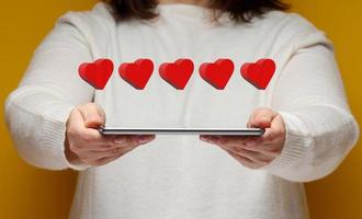 woman holds an electronic tablet and five red hearts over it. Feedback concept, business rating photo