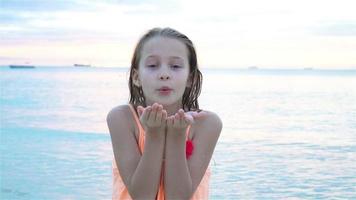 Adorable little girl at beach having a lot of fun in the evening. Happy kid looking at camera background beautiful sky and sea video