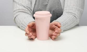 mujer en gris ropa sostiene un rosado cerámico taza, mujer se sienta a un blanco mesa, comienzo de el día, Mañana foto