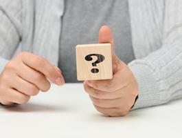 mano femenina sosteniendo un cubo de madera con un signo de interrogación, concepto de respuestas y preguntas, suspenso y métodos de solución foto