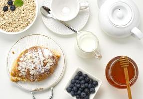 Raw oatmeal in white ceramic plate, blueberry, honey on white table, breakfast photo