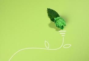 a crumpled sheet of paper and a green leaf on a green background, the shape of a light bulb. Energy saving concept, new creative idea photo
