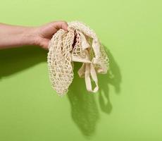 female hand holds empty green reusable string bag woven from thread on a green background, zero waste photo