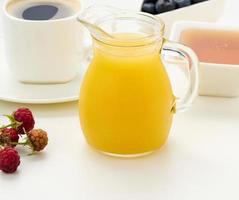 recién exprimido jugo en un vaso transparente licorera, un taza de café, miel en un blanco mesa. Mañana desayuno foto