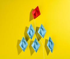 group of blue paper boats and one red led on a yellow background. photo