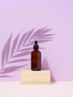 Brown glass bottle with a pipette on purple background. Palm leaf shadow photo