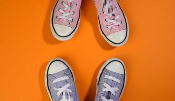 two pairs of textile sneakers on an orange background stand opposite each other. Dialogue and confrontation concept photo