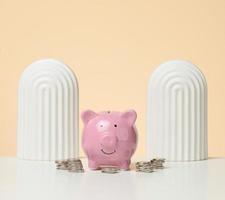 coins and pink piggy bank on a white table. Concept of accumulating cash, saving, receiving subsidies photo