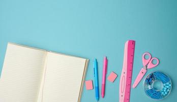 open notebook with blank pink sheets, scissors and ruler on blue background, top view photo
