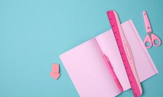 open notebook with blank pink sheets, scissors and ruler on blue background, top view photo