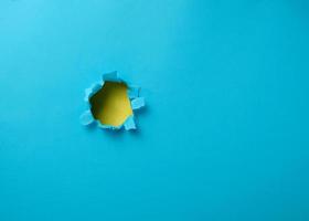 hole with torn edges in blue paper, full frame photo