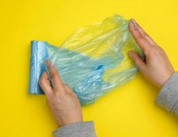 female hand unwinds a blue plastic bag for rubbish, yellow background photo