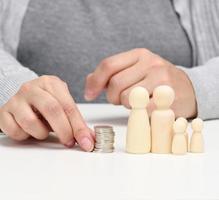 hand puts coins in a pile and wooden figurines of a family on a white table. Economy and investment concept, budget planning. Receiving subsidies from the state photo