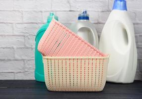 botellas con detergente líquido y cestas de ropa vacías de plástico sobre una mesa azul de madera foto