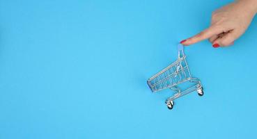 female hands hold an empty metal miniature trolley on a blue background. Sale concept photo