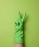 hand in a rubber green glove for cleaning on a green background, part of the body is raised up photo