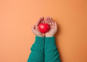 female hands holds red heart, orange background. Love and donation concept photo