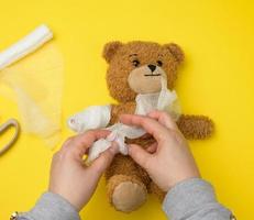 funny vintage brown curly teddy bear with rewound paw with white gauze bandage photo