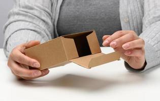 two female hands hold a square box made of brown corrugated cardboard on a white background, close up photo