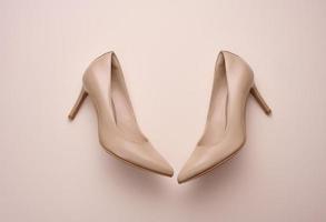 leather beige high heel shoes on a beige background, top view photo