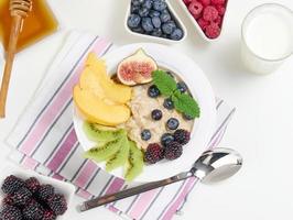 milk, plate with oatmeal porridge and fruit, honey in a bowl on a white table. Healthy breakfast photo