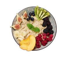 boiled oatmeal with fruits in a round plate on a white isolated background, top view photo