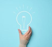 Woman's hand and a drawn electric lamp on a blue background. The concept of searching for ideas and solutions, brainstorming. Switching to alternative forms of energy photo