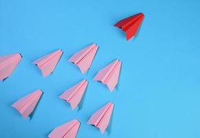 a group of pink paper planes follow the first red against a blue background photo