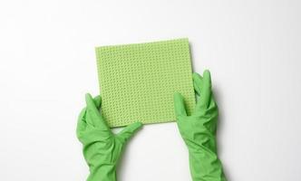 la mano en un guante de goma verde sostiene una esponja suave para limpiar superficies sobre un fondo blanco foto