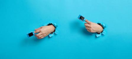 an oximeter for measuring oxygen in the blood is worn on the index finger, part of the hand is sticking out of a torn hole in the blue paper photo