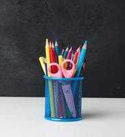 metal glass with pens, pencils and felt-tip pens and scissors on the background of an empty black chalk board photo