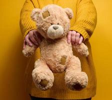 woman in orange knitted sweater hugs cute brown teddy bear. photo