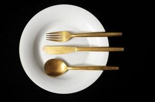 Fork, spoon and a knife on a plate on black background photo