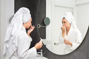 Female in bathrobe applying cream against mirror photo