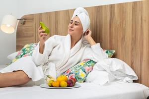 Smiling woman relaxing on bed eating pear photo