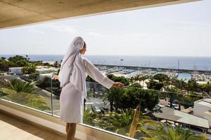 Woman in bathrobe standing on balcony enjoying view of tropical resort photo