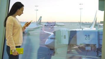 Portrait of young woman with smartphone in international airport. Airline passenger in an airport lounge waiting for flight aircraft video