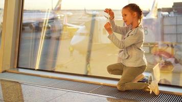 adorável pequeno menina jogando com pequeno modelo avião dentro aeroporto esperando para embarque. conceito do vôo e avião. video