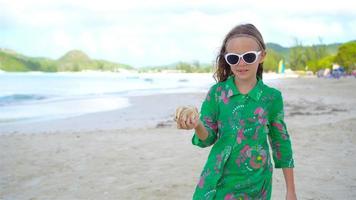 niña linda con concha en las manos en la playa tropical. adorable niña jugando con conchas marinas en la playa video