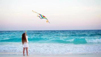 liten flicka med flygande drake på tropisk strand på solnedgång. unge spela på hav Strand. barn med strand leksaker. video