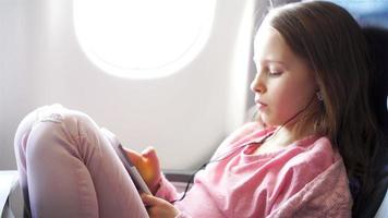 Adorable little girl traveling by an airplane. Cute kid with laptop near window in aircraft video