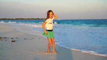 bezaubernd glücklich wenig Mädchen auf Weiß Strand beim Sonnenuntergang. süß Kind tanzen auf das tropisch Strand im schleppend Bewegung Video