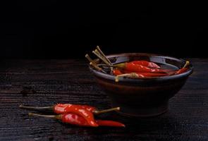 Pickled chili peppers in a clay cup on a wooden board. photo