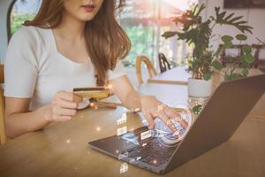 Young Asian woman holding credit card and using laptop computer. Beautiful happy young girl in cafe. Online shopping, E-commerce, spending money, technology money wallet and online payment concept. photo