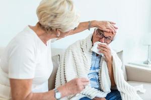 Older woman helps a ill husband while they are sitting on the couch in the living room. Senior man with flu and running nose. photo