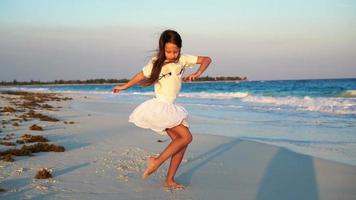 Adorable happy little girl on white beach at sunset. Cute kid dance on the tropical seashore in slow motion video