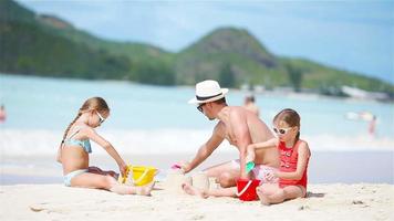 Family making sand castle at tropical white beach. Father and two girls playing with sand on tropical beach video